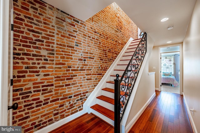 stairway with brick wall, hardwood / wood-style floors, recessed lighting, and baseboards