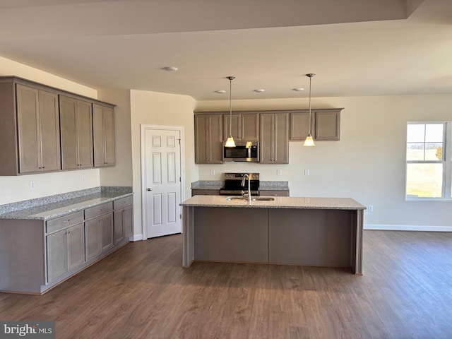 kitchen featuring stainless steel appliances, decorative light fixtures, a sink, and light stone counters