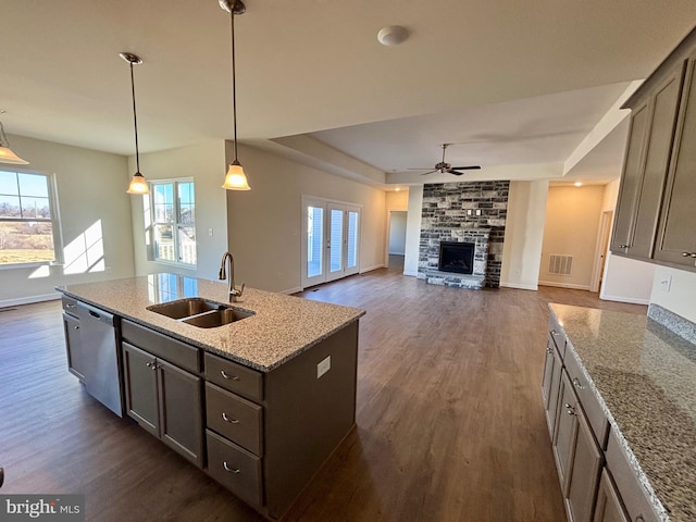 kitchen with a kitchen island with sink, a sink, hanging light fixtures, stainless steel dishwasher, and light stone countertops