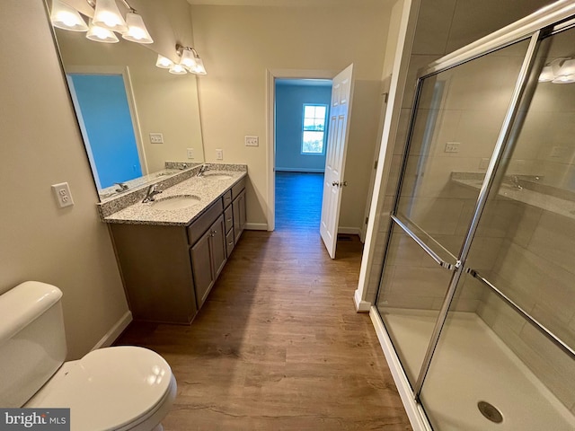 bathroom with double vanity, wood finished floors, a sink, and a shower stall