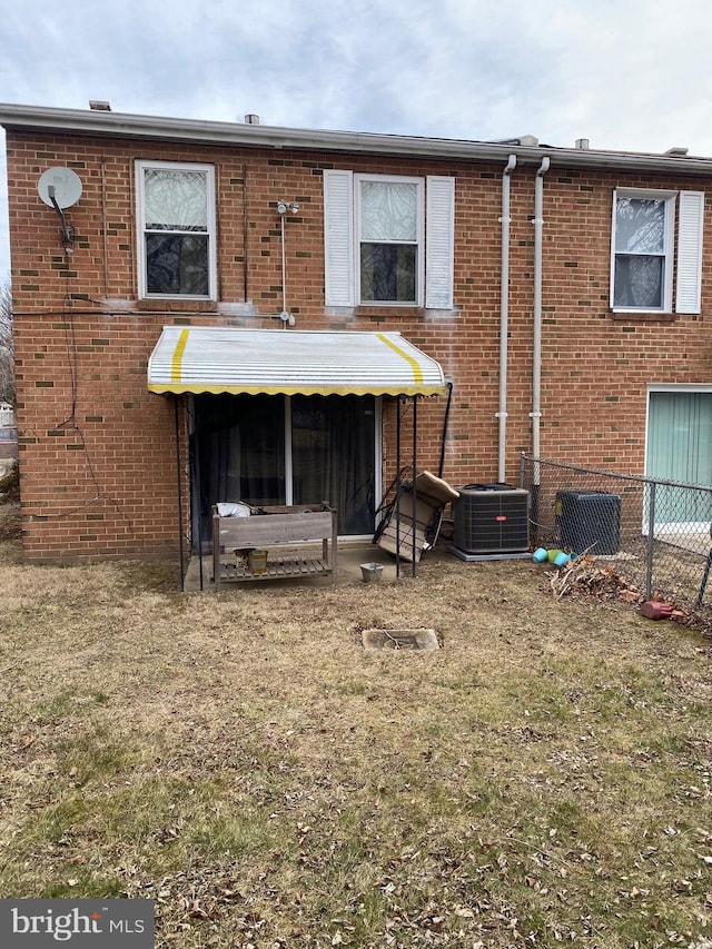 rear view of property with brick siding, a lawn, and fence