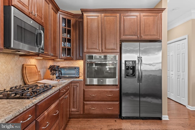 kitchen featuring a toaster, crown molding, light wood finished floors, appliances with stainless steel finishes, and glass insert cabinets