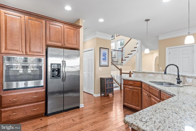 kitchen featuring brown cabinetry, crown molding, stainless steel appliances, and a sink