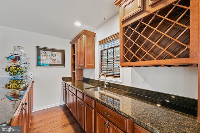 kitchen featuring light wood finished floors, baseboards, dark stone counters, a sink, and recessed lighting