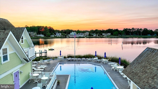 pool at dusk featuring a water view, a community pool, and a patio