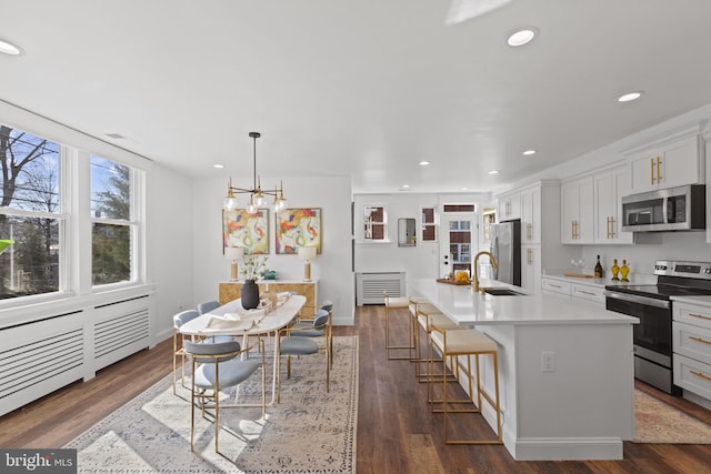 kitchen featuring a kitchen island with sink, stainless steel appliances, dark wood-type flooring, a kitchen breakfast bar, and light countertops