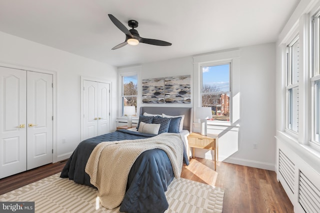 bedroom with ceiling fan, two closets, baseboards, and wood finished floors