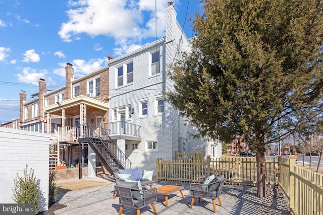 back of property with brick siding, a patio, a chimney, fence, and stairs