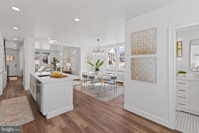 kitchen featuring light countertops, stainless steel dishwasher, a sink, and dark wood finished floors