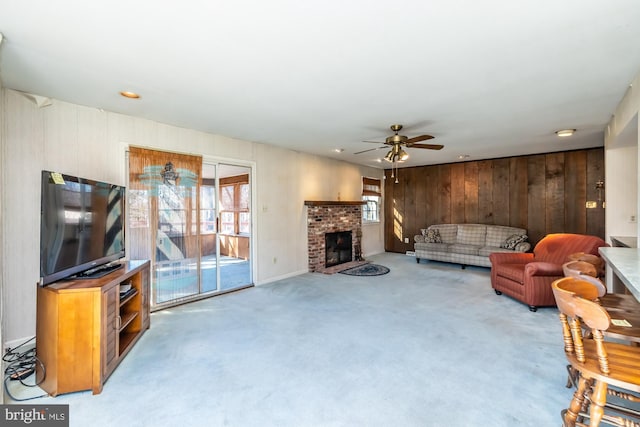 living area with ceiling fan, wood walls, carpet, and a brick fireplace