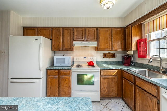 kitchen with white appliances, brown cabinets, under cabinet range hood, a sink, and light tile patterned flooring