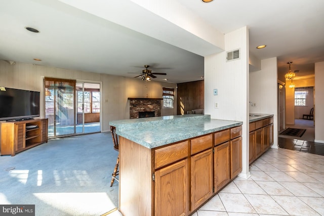 kitchen featuring visible vents, a ceiling fan, a brick fireplace, open floor plan, and a kitchen bar