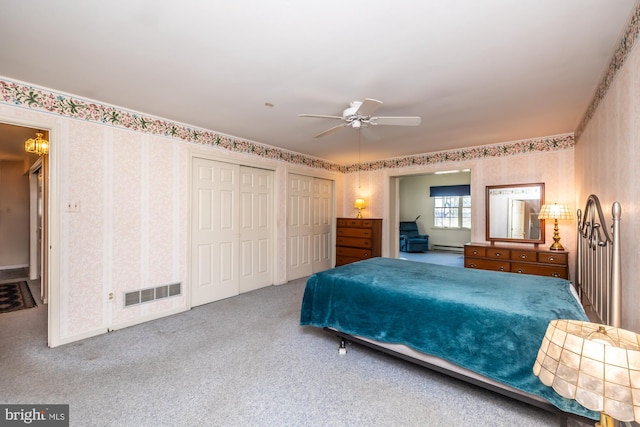 carpeted bedroom with wallpapered walls, visible vents, and multiple closets