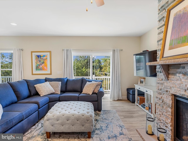 living room with ceiling fan, a stone fireplace, recessed lighting, and light wood-style floors