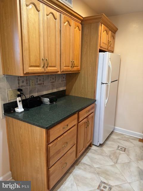 kitchen with baseboards, decorative backsplash, freestanding refrigerator, brown cabinets, and dark countertops