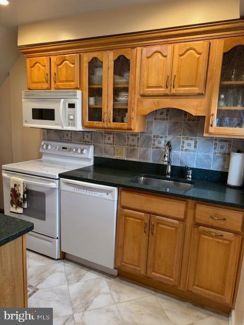 kitchen with white appliances, decorative backsplash, brown cabinetry, and a sink