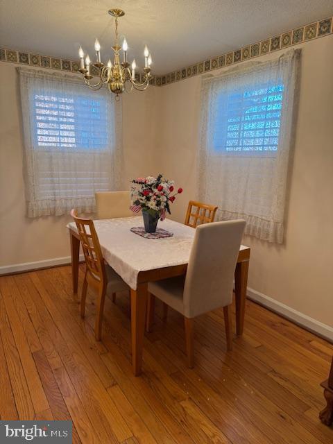 dining room with a notable chandelier, a textured ceiling, hardwood / wood-style flooring, and baseboards