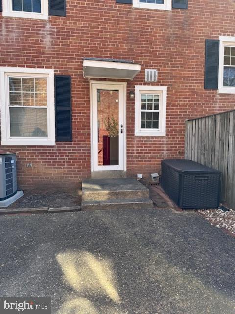 view of exterior entry featuring fence, cooling unit, and brick siding