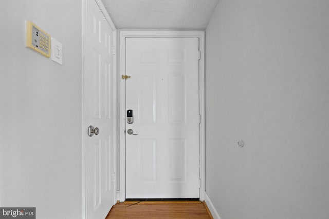 doorway with baseboards, a textured ceiling, and wood finished floors