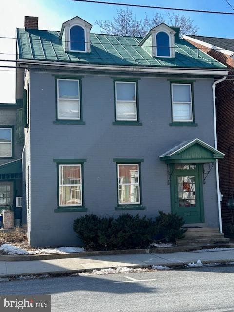 view of front facade featuring cooling unit, brick siding, and a chimney