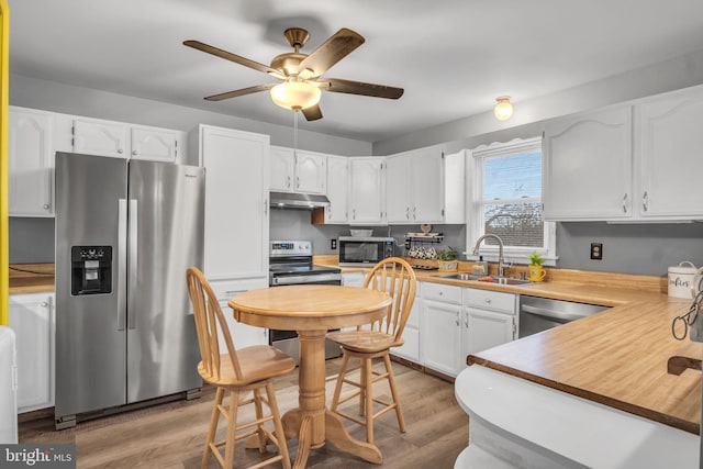 kitchen with light wood-style flooring, under cabinet range hood, a sink, white cabinetry, and appliances with stainless steel finishes