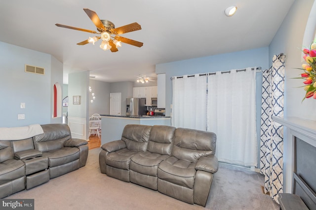 living area featuring ceiling fan, visible vents, and light colored carpet