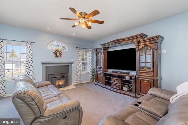 living area with a glass covered fireplace, light colored carpet, ceiling fan, and baseboards