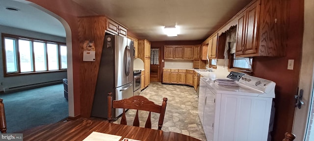 kitchen featuring arched walkways, a baseboard radiator, stainless steel appliances, a sink, and washing machine and clothes dryer