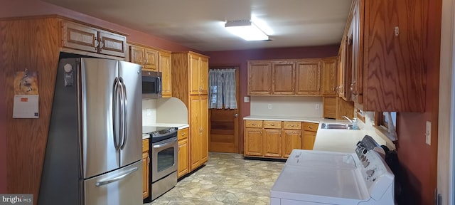 kitchen with washer / dryer, brown cabinetry, stainless steel appliances, light countertops, and a sink