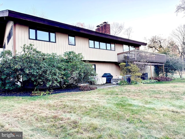 back of property featuring a chimney, a lawn, and a wooden deck