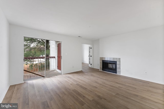 unfurnished living room featuring a tiled fireplace, wood finished floors, visible vents, and baseboards