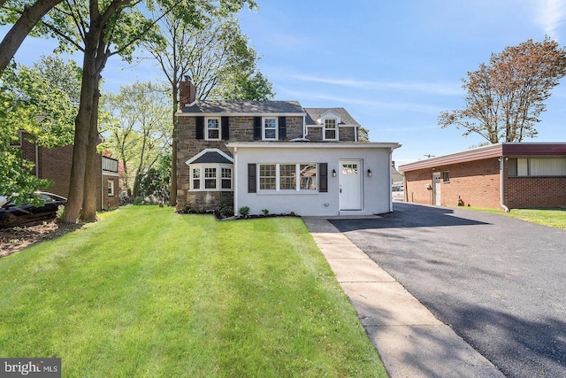 view of front of house with driveway, stone siding, a chimney, a front lawn, and stucco siding