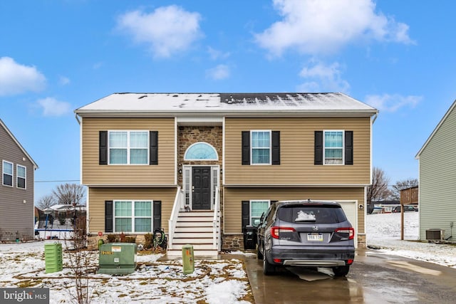 raised ranch featuring a garage, concrete driveway, and central AC unit