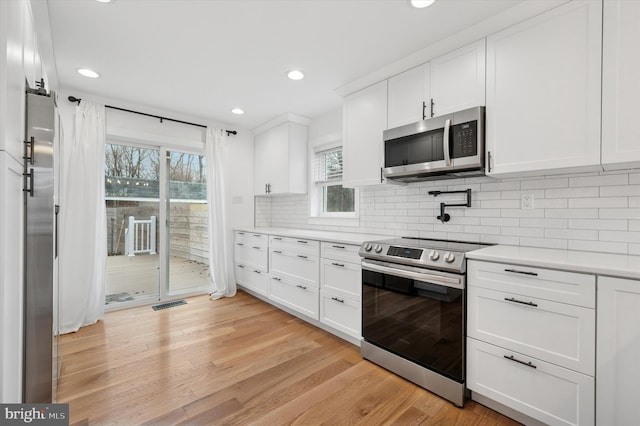 kitchen featuring white cabinets, stainless steel appliances, light countertops, light wood-style floors, and backsplash