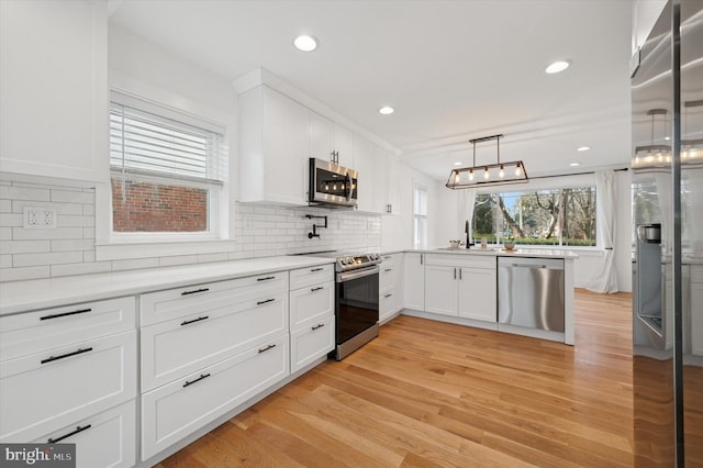 kitchen featuring appliances with stainless steel finishes, light countertops, light wood-style floors, white cabinetry, and a sink