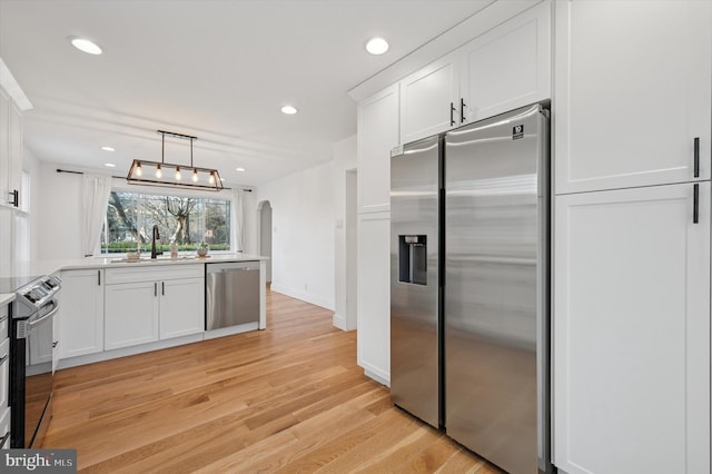 kitchen featuring arched walkways, white cabinets, appliances with stainless steel finishes, light countertops, and a sink