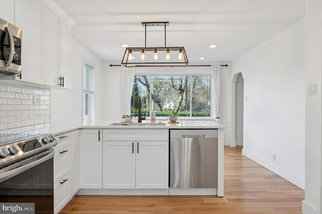 kitchen featuring stainless steel appliances, light countertops, white cabinetry, and hanging light fixtures