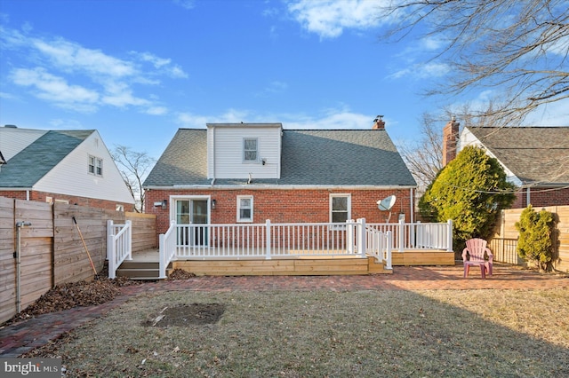 rear view of house featuring roof with shingles, brick siding, a lawn, and a wooden deck