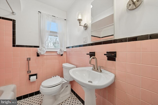 bathroom featuring tile walls, wainscoting, toilet, tile patterned flooring, and a sink