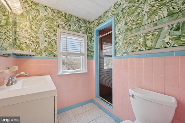 bathroom featuring toilet, wallpapered walls, a shower stall, and wainscoting