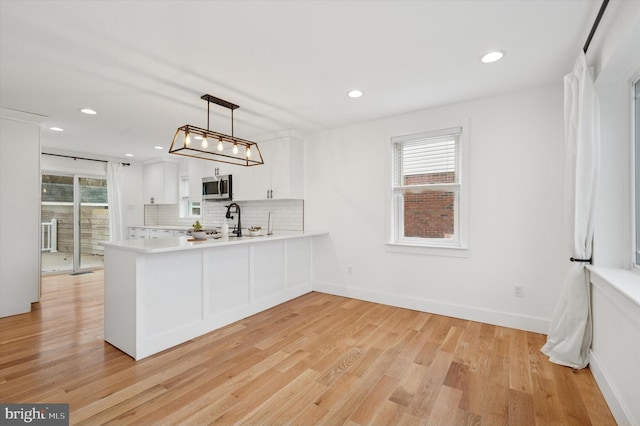 kitchen with a peninsula, white cabinetry, stainless steel microwave, and light countertops