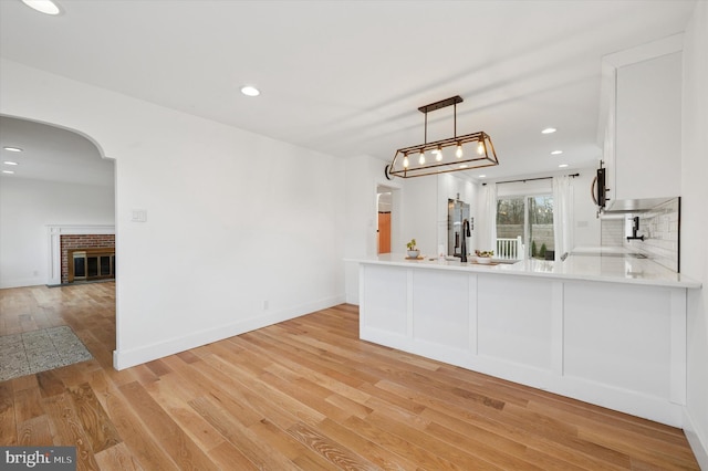 kitchen with pendant lighting, a peninsula, light countertops, white cabinetry, and stainless steel refrigerator with ice dispenser