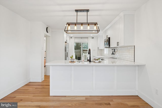 kitchen with appliances with stainless steel finishes, a peninsula, light countertops, pendant lighting, and backsplash