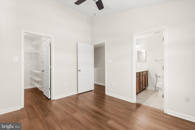 unfurnished bedroom with baseboards, light wood-style floors, a spacious closet, a closet, and ensuite bath