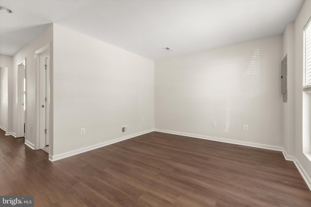 empty room with dark wood-style floors, electric panel, visible vents, and baseboards