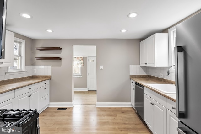 kitchen with a sink, light wood-style floors, white cabinets, dishwasher, and tasteful backsplash