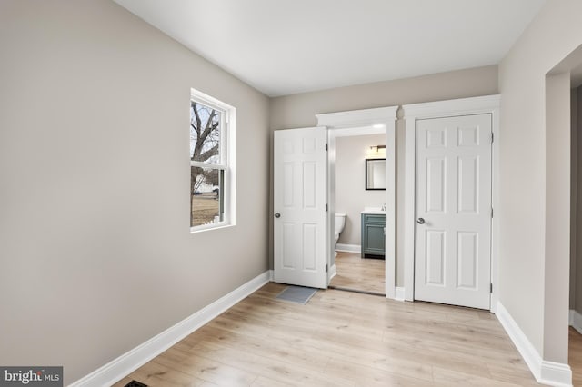 unfurnished bedroom featuring light wood finished floors, ensuite bath, and baseboards