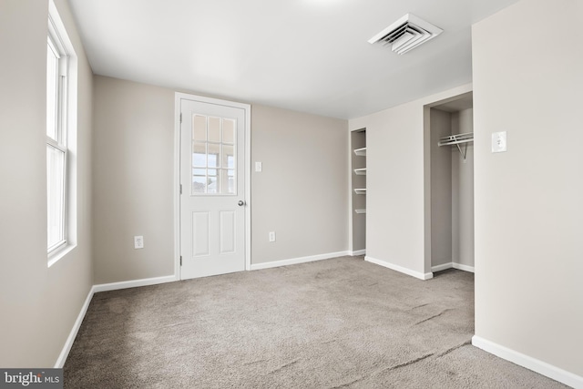 unfurnished bedroom featuring carpet floors, baseboards, multiple windows, and visible vents