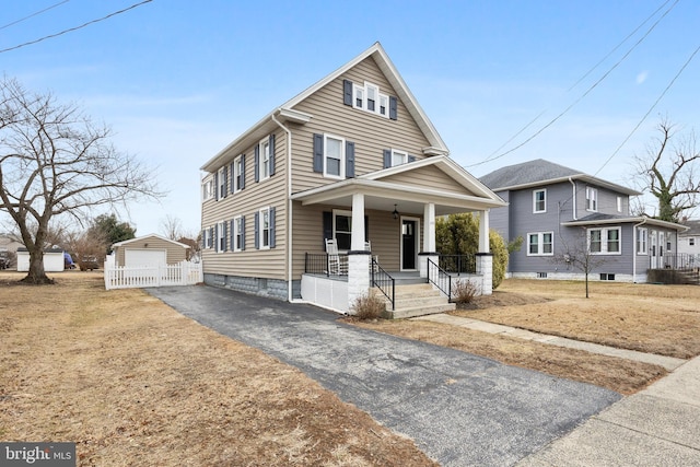 view of front of property featuring aphalt driveway, an outbuilding, covered porch, a front yard, and a garage