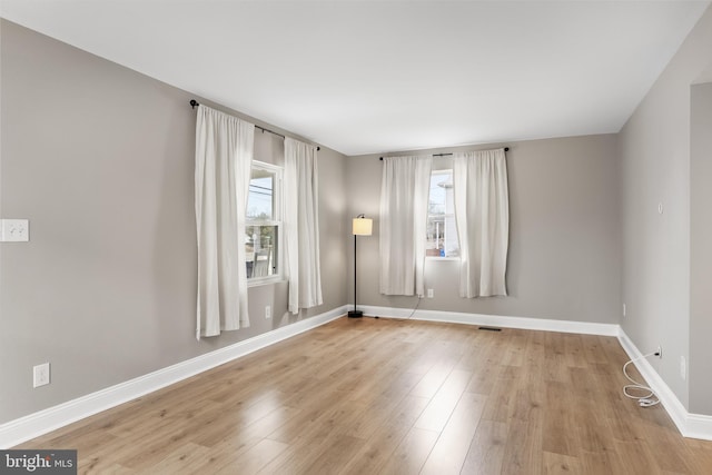 spare room featuring light wood-style floors, a healthy amount of sunlight, visible vents, and baseboards